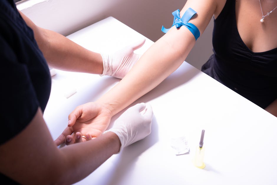 Healthcare worker in gloves draws blood from a patient’s forearm; a blue ribbon is tied on the arm.